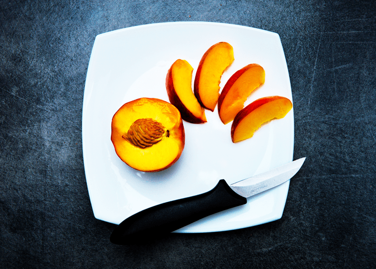 white plate on a black table on which lies a knife and sliced peach