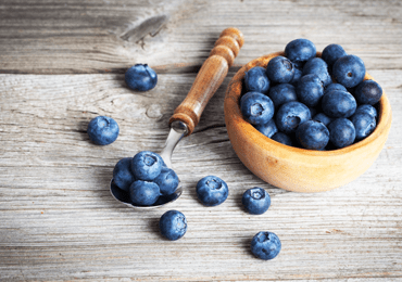 A wooden bowl filled with berries next to which lies a small teaspoon