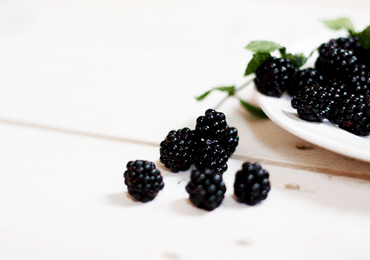 a piece of white plate filled with blackberries, some of which fell on the table