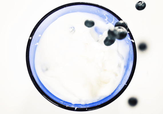 Viewed from above a glass of milk to which blueberries fall